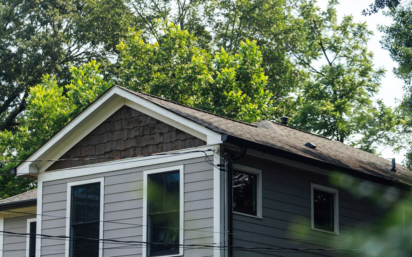 A two-storey house clad in grey lap siding with white trim and a cedar-shingled gable