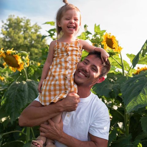 Jake Martin, the owner of Elite Carpentry, smiling outdoors in a
                      sunflower field with a young child on his shoulder.